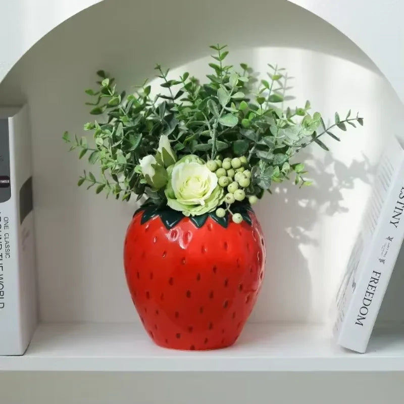 Jarrón de cerámica con flor de fresa, follaje verde y rosas blancas, en una nicho blanca.