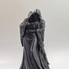 A dark, flowing statue of a figure with a hood embracing their face.