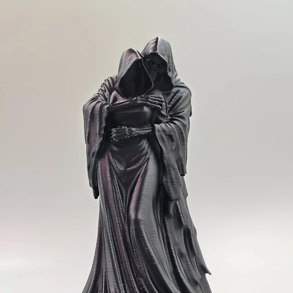 A dark, flowing statue of a figure with a hood embracing their face.