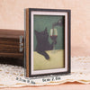 Gerahmtes Bild einer schwarzen Katze, die ein Glas Rotwein hält, auf einer hellen Oberfläche.