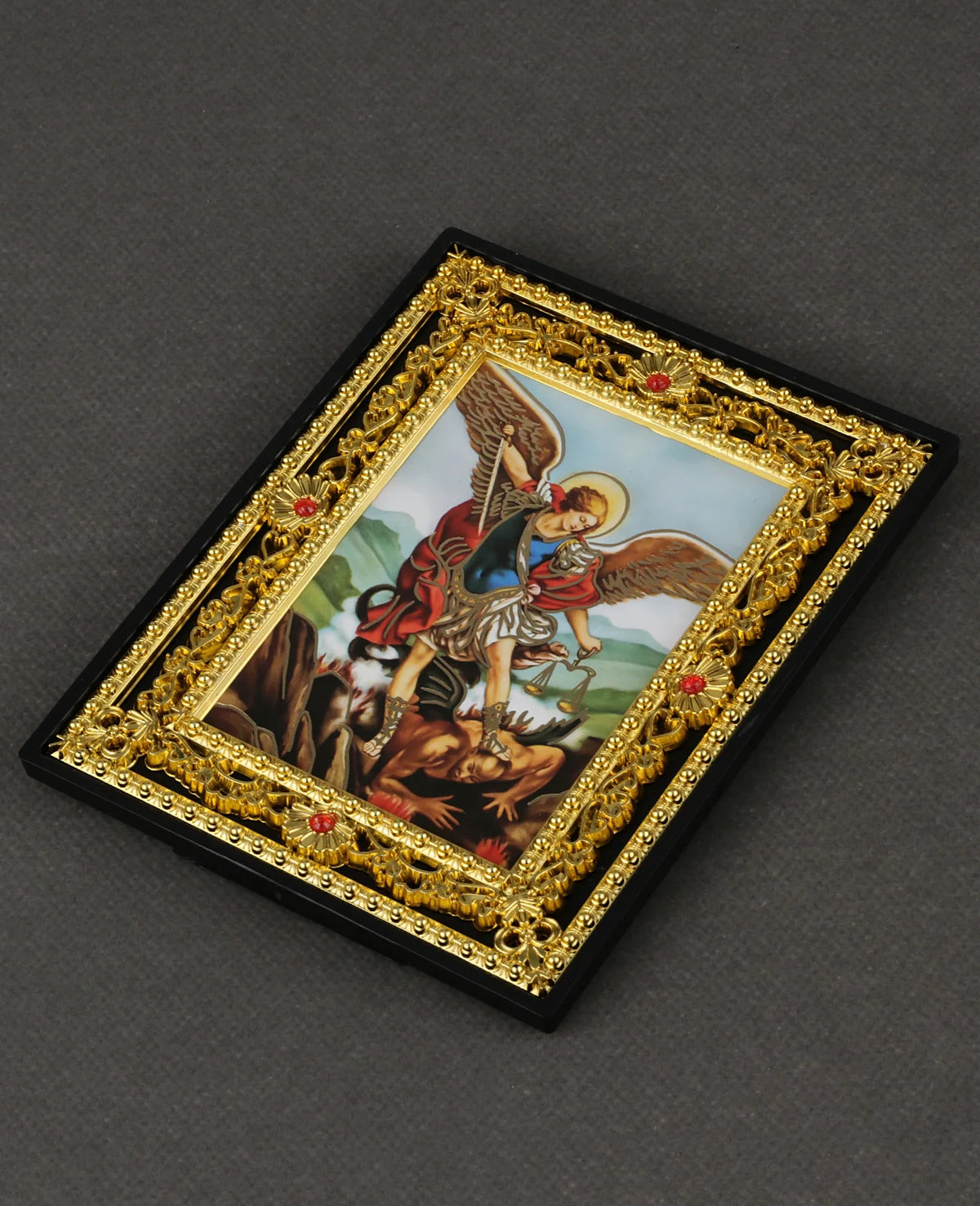 A framed icon depicting the Catholic Holy Family with an archangel, set in a gold-edged black frame.