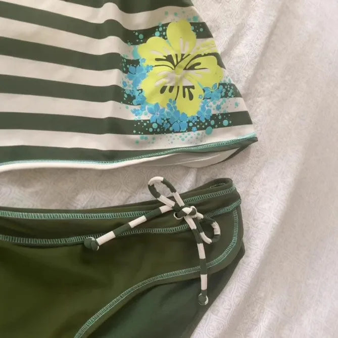 A striped sleeveless top featuring a white and dark green pattern with yellow and blue floral accents.