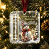 Clear acrylic ornament featuring a snowman and Christmas theme with a velvet ribbon hanging on a festive green tree branch.