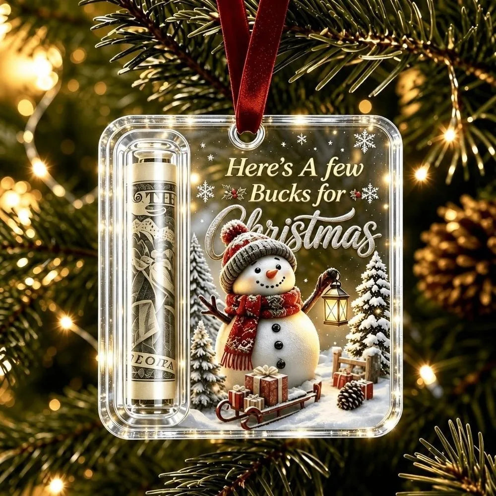 Clear acrylic ornament featuring a snowman and Christmas theme with a velvet ribbon hanging on a festive green tree branch.