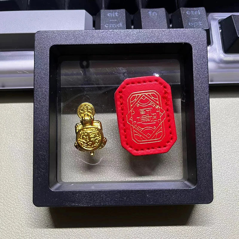 A golden tortoise figurine is displayed in a black square box on a keyboard surface.
