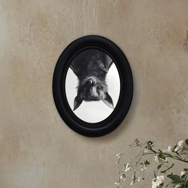 A framed photograph of a dark bat's head hanging on a beige wall.