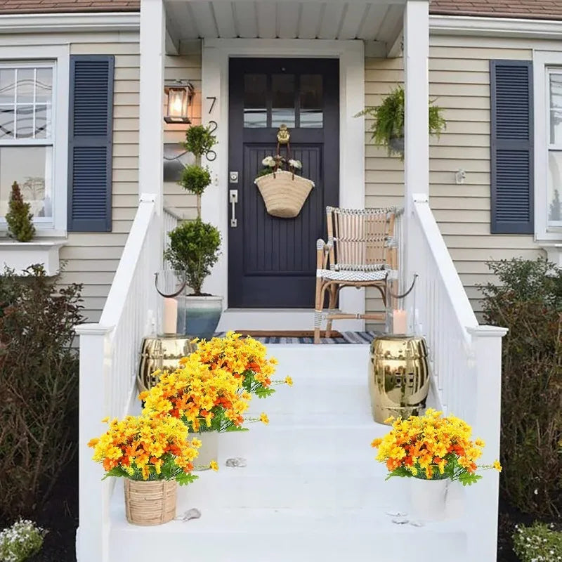 A white staircase decorated with yellow artificial daisy flowers and potted greenery in front of a dark gray house entrance.