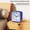 A blue quartz small alarm clock with a night light is displayed on a wooden bedside table.