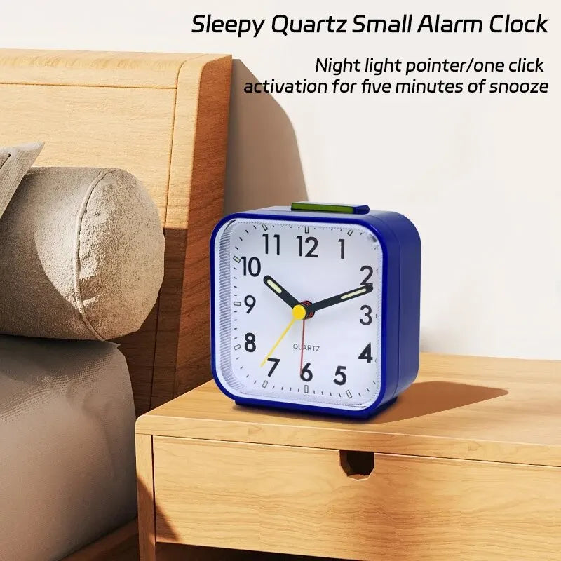 A blue quartz small alarm clock with a night light is displayed on a wooden bedside table.
