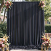 A dark gray fabric backdrop curtain with vertical pleats decorated with floral arrangements.