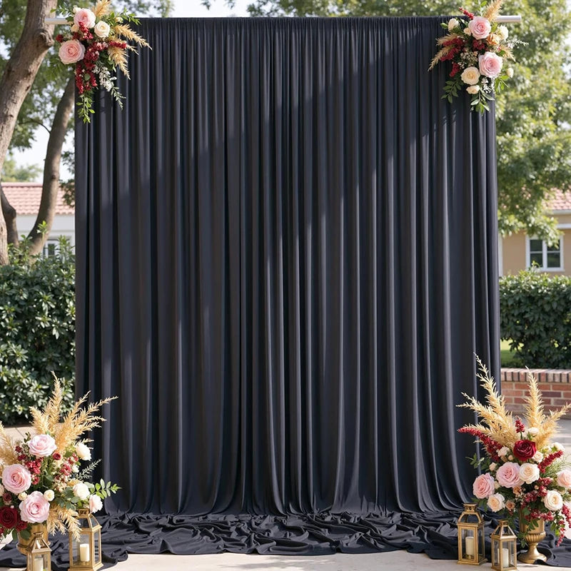 A dark gray fabric backdrop curtain with vertical pleats decorated with floral arrangements.