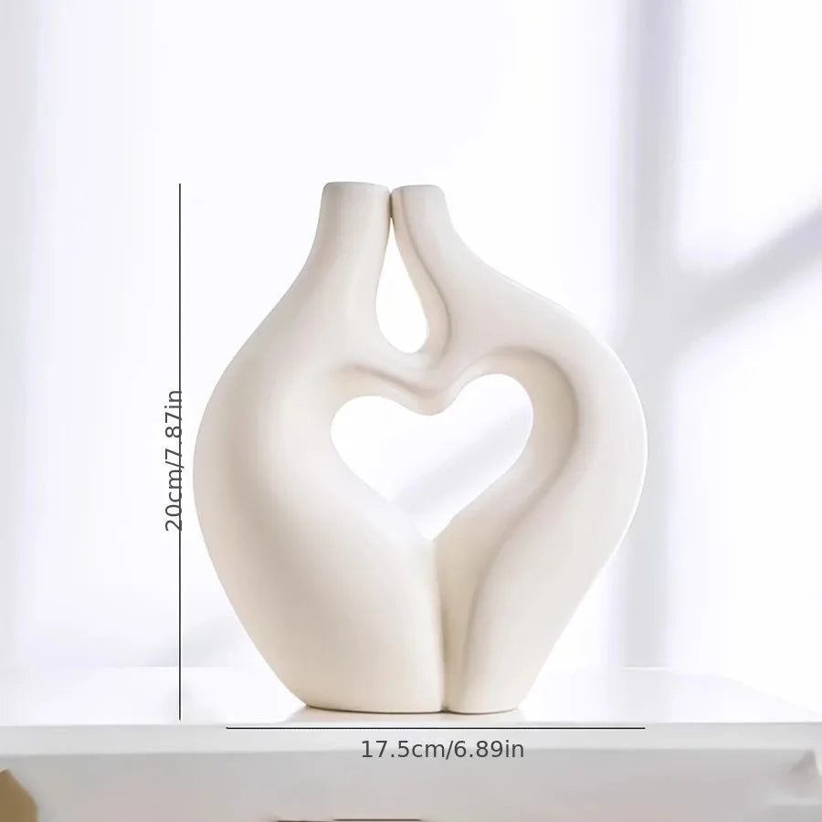 A smooth, white, heart-shaped vase or sculpture is shown against a bright background.
