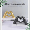 Gold and black heart-shaped resin hand sculptures used as decorative ornaments on a white surface.