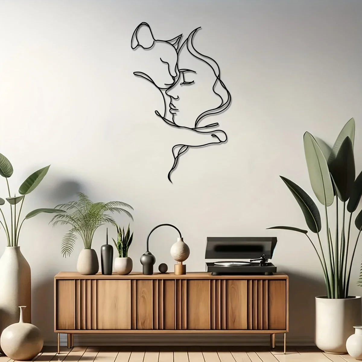Minimalist metal silhouette art of a cat and woman against a light gray wall above a wooden cabinet.