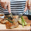 A person uses a disposable plastic silverware set to serve food on a wooden board.