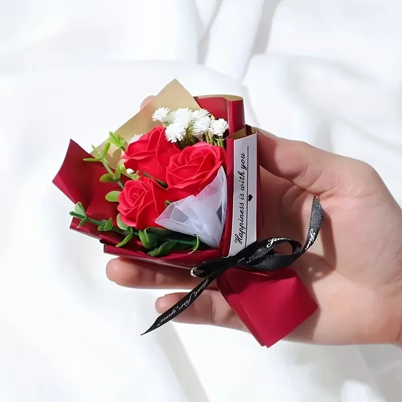 Une main tient une boîte cadeau rouge contenant des mini roses artificielles et une note manuscrite.