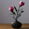 A pink rose branch in a dark vase on a wooden surface.
