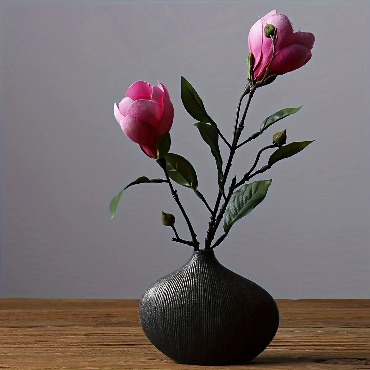 A pink rose branch in a dark vase on a wooden surface.