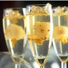 A close-up of a champagne flute filled with sparkling wine and edible gold leaf flakes for decoration.