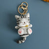 A handcrafted crochet cat keychain pendant with gray and black stripes and a gold ring.