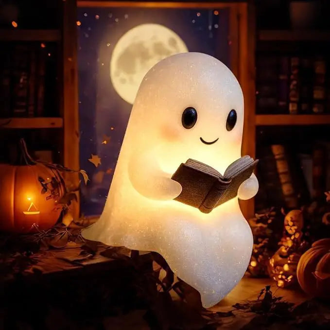 A white ghost figurine lamp with a warm glow sits on a wooden surface next to autumn decorations.