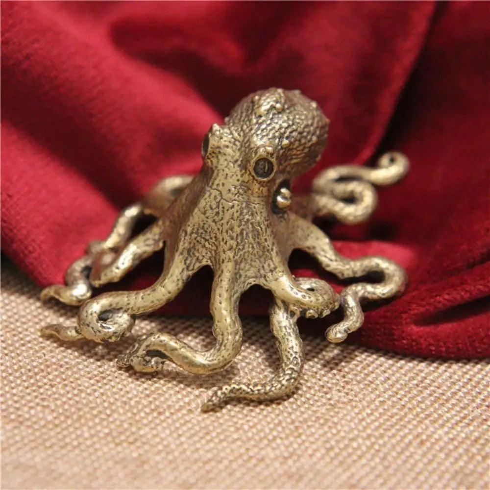 Antique brass octopus desk ornament resting on a red fabric background.
