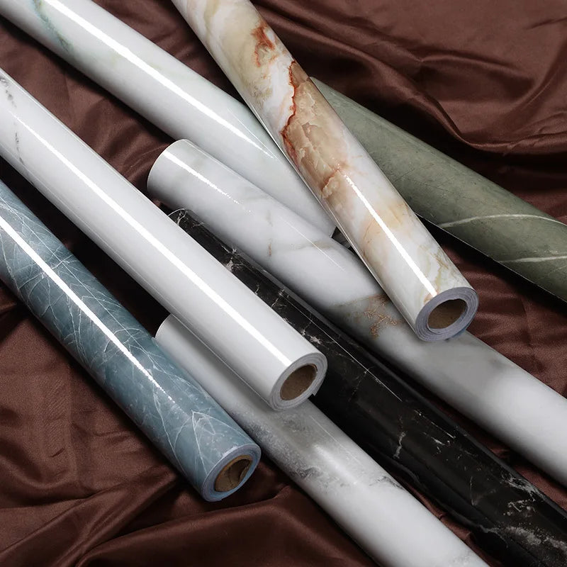 Rolls of self-adhesive marble contact paper in various colors and patterns lying on brown fabric.