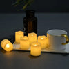A set of glowing yellow LED tea light candles arranged on a white tray next to a dark glass bottle and a white mug.