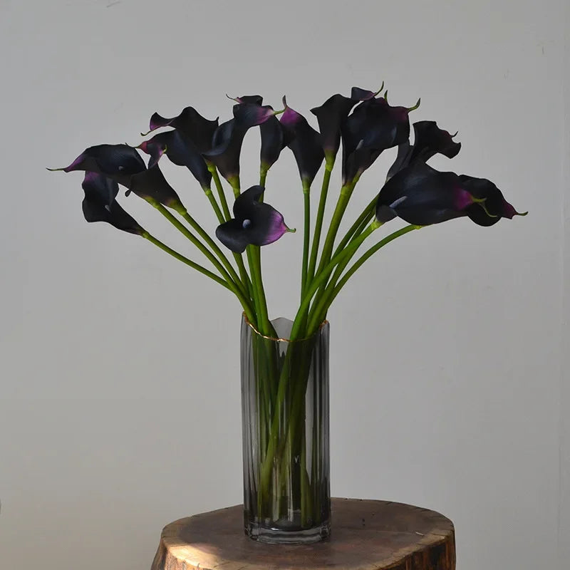 A bouquet of dark purple and black EVA artificial calla lily stems in a glass vase.