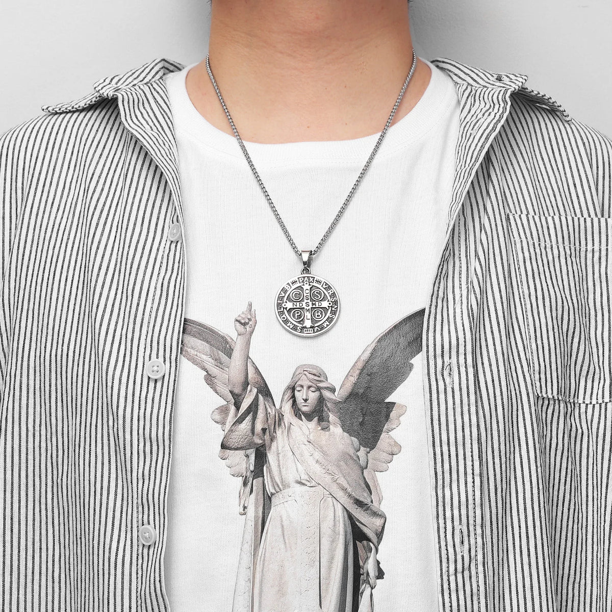 A stainless steel punk cross necklace with an intricate design is worn over a striped shirt.