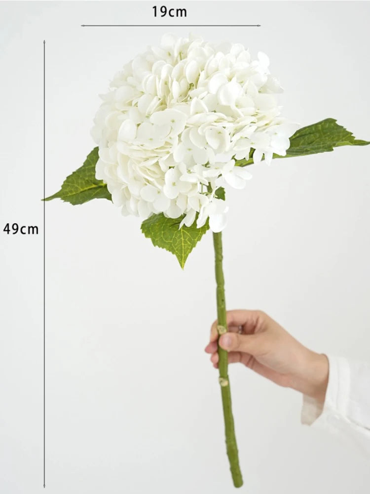 A white hydrangea silk flower branch with green leaves is shown being held, measuring 19cm in height.