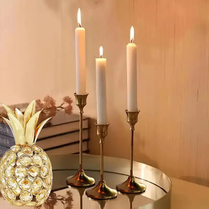 A set of three matte gold taper candle holders with white candles displayed on a table.