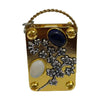 A small gold-toned metal box with a braided handle, featuring pressed dried flowers and a blue stone.