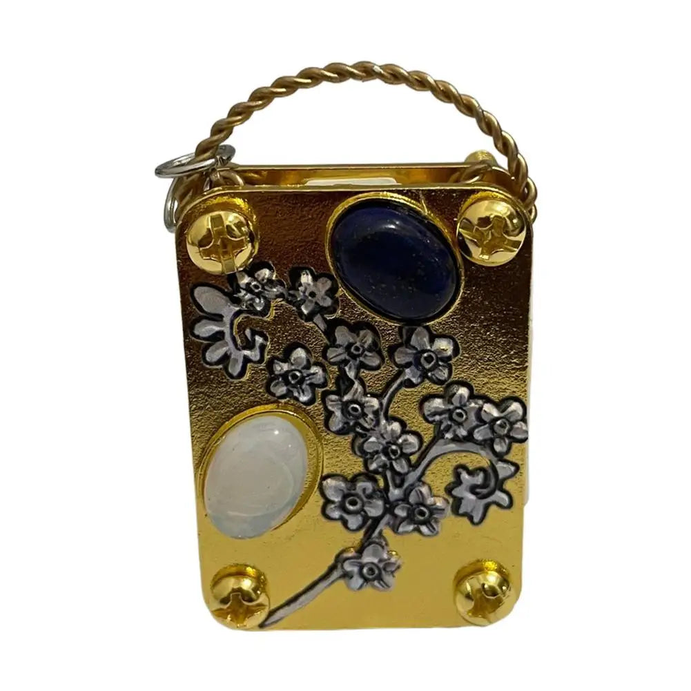 A small gold-toned metal box with a braided handle, featuring pressed dried flowers and a blue stone.
