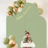 A photo of a green backdrop with gold balloons and a child wearing a party hat.