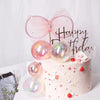 A pink cake decorated with iridescent clear balloons and a sparkly pink bow topper for a birthday celebration.