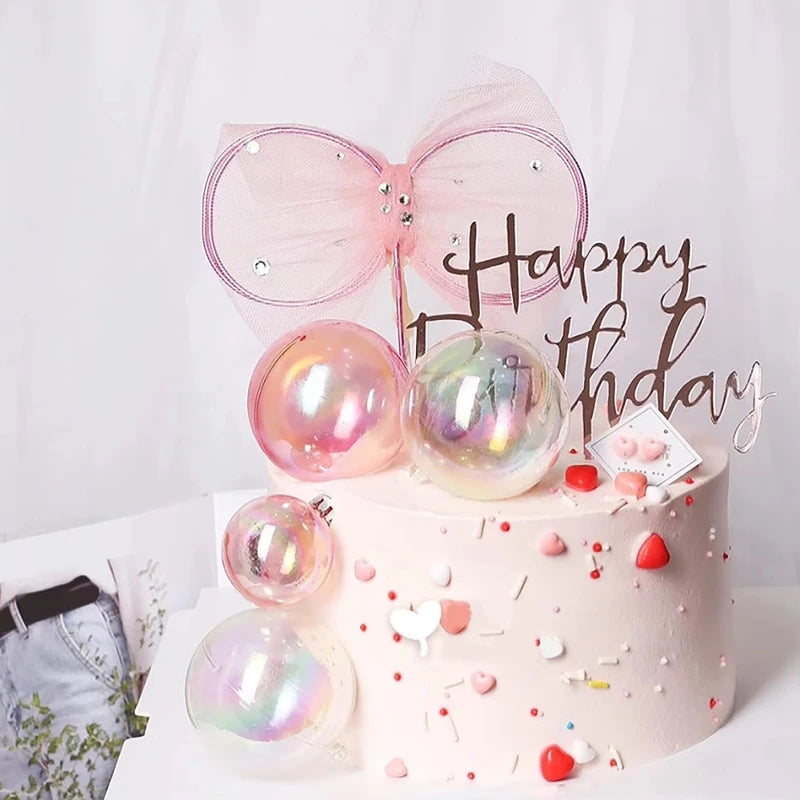 A pink cake decorated with iridescent clear balloons and a sparkly pink bow topper for a birthday celebration.