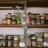 Stainless steel canning jar lifter with non-slip grip hanging on a wooden shelf filled with various jars.