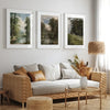 A gallery wall featuring three framed landscape paintings of nature and trees on a white wall.
