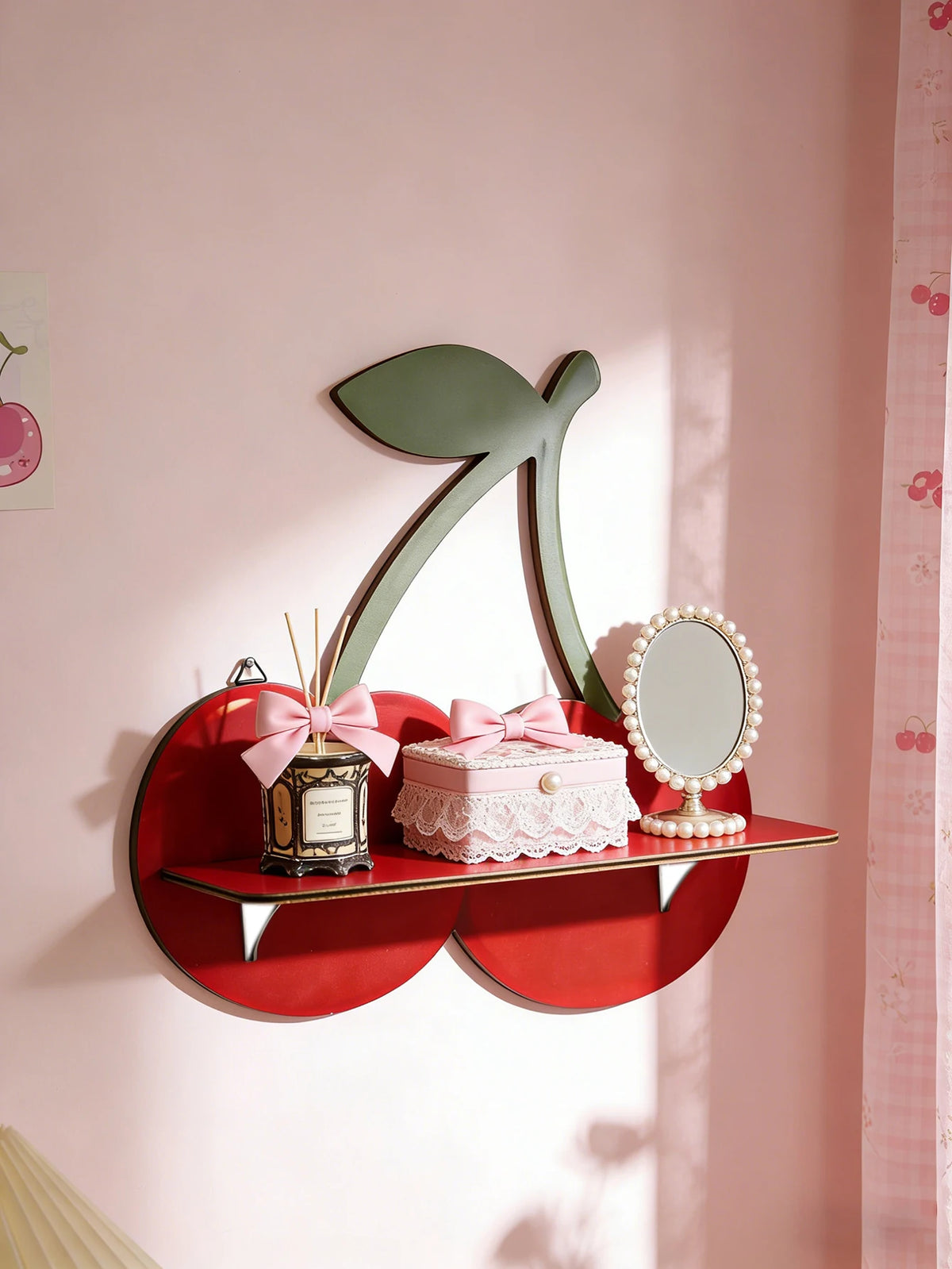 A red wooden shelf with a large green cherry-shaped cutout displaying a pink gift box and a silver mirror.