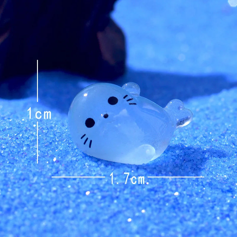 A translucent blue glow in the dark resin sea animal figurine with a black cat face, resting on a blue surface.