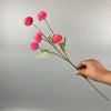 Una mano sostiene un tallo de flores artificiales de margarita de crisantemo rosa contra un fondo gris claro.