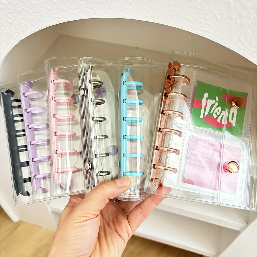 A hand holds an acrylic binder filled with pastel macaron-themed plastic sleeves and various decorative charms.