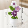 Hand woven crochet flowers in purple and white are potted in a white ceramic container.
