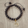 A black beaded bracelet with a gold zodiac charm is displayed on a wooden surface.