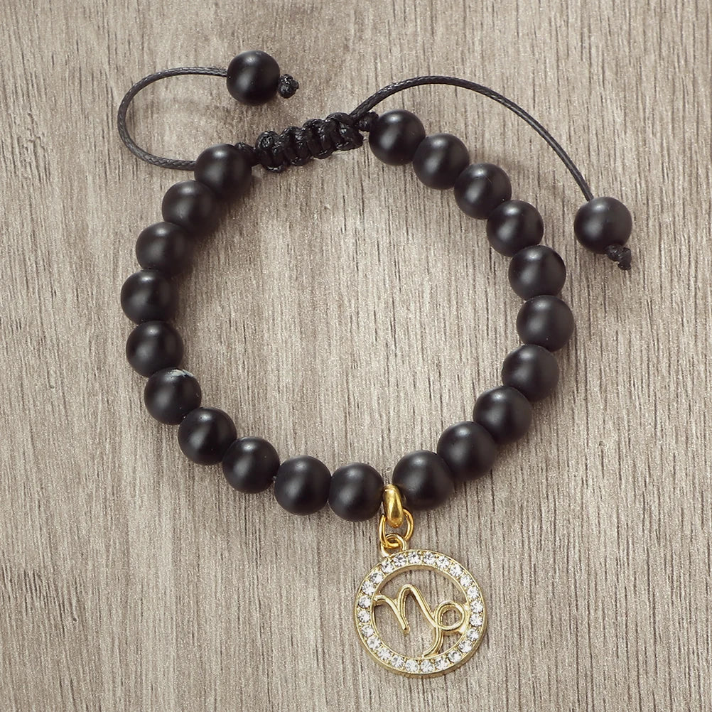A black beaded bracelet with a gold zodiac charm is displayed on a wooden surface.