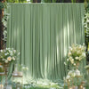 A soft sage green fabric backdrop with vertical pleats decorated with white flowers and greenery for an event.