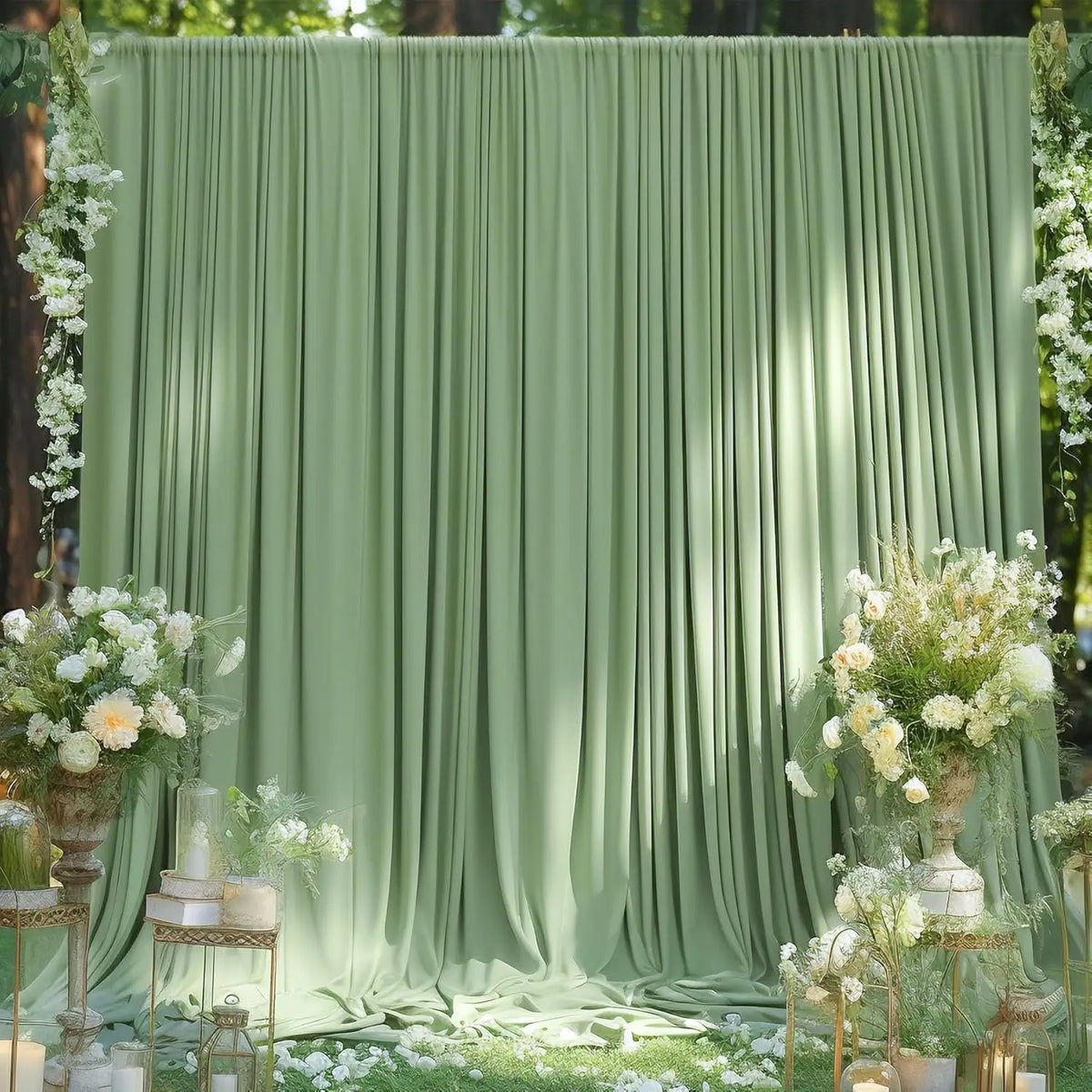 A soft sage green fabric backdrop with vertical pleats decorated with white flowers and greenery for an event.