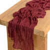 A deep burgundy gauze table runner draped over a light wood surface.