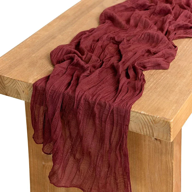 A deep burgundy gauze table runner draped over a light wood surface.